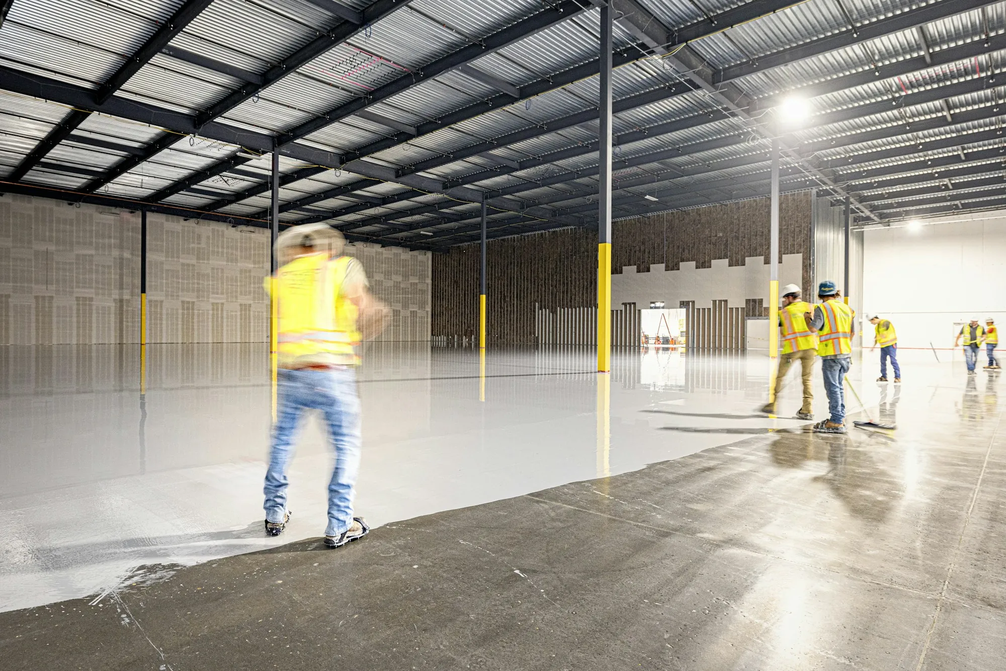 Workers scrubbing the floor of a large, empty warehouse